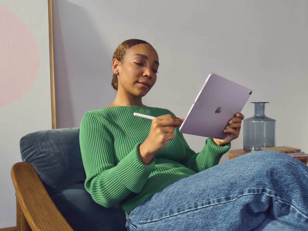 A person relaxing in a chair with the new iPad Air and an Apple Pencil