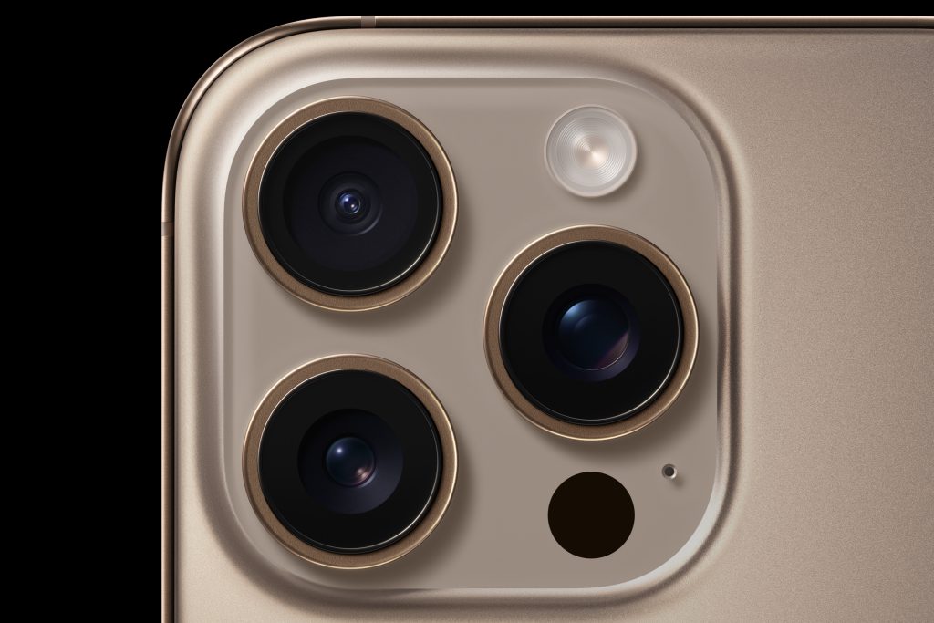 A closeup of the iPhone 16 Pro's camera system, the phone is Desert Titanium on a black background