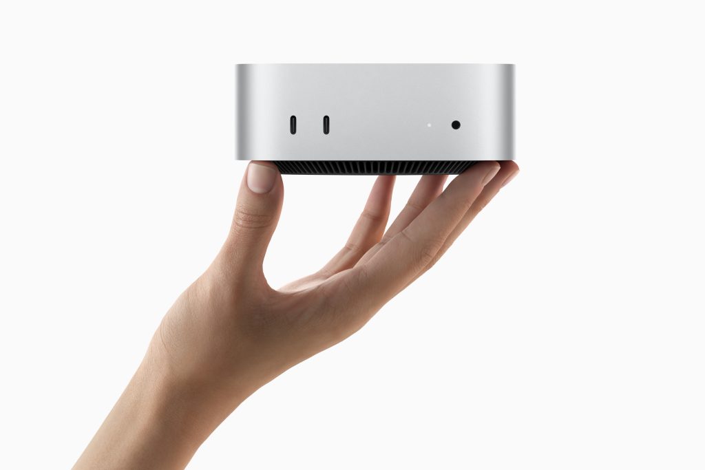 A Mac mini being held in a person's hand on a white background