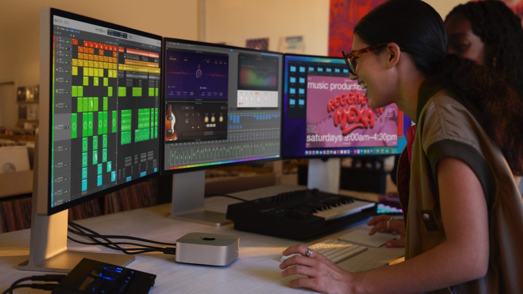 Two people using the M4 Mac mini with three Studio Displays and a MIDI keyboard